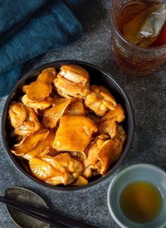 a bowl filled with chicken next to chopsticks and a cup of tea