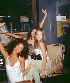 three young women posing for the camera with their arms in the air while sitting on a chair