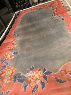 an orange and blue table cloth with flowers on it, sitting on a metal stand