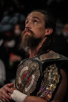 a man with a beard standing in front of a crowd wearing a wrestling ring belt