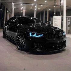 a black bmw car parked in front of a building at night with its lights on