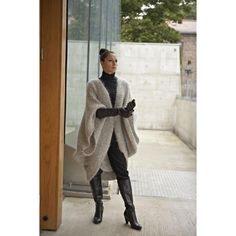 a woman standing in front of a glass door wearing black boots and a gray cardigan