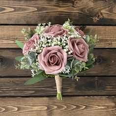 a bouquet of pink roses and baby's breath on a wooden background with greenery