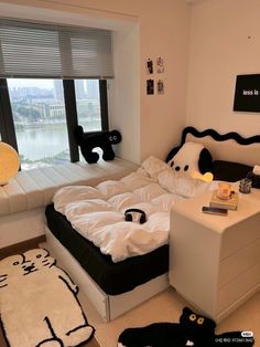 a bed with white sheets and black pillows in a bedroom next to a large window