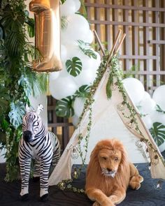 two stuffed animals sitting in front of a teepee with balloons and greenery on it