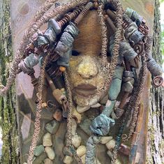 a sculpture made out of rocks and chains on a tree trunk with a face in the middle