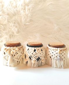 three crocheted jars with wooden lids and tassels on white furnishing