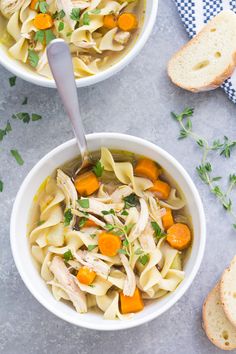 two bowls of chicken noodle soup with bread on the side