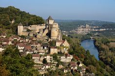 an old castle perched on top of a hill next to a river in the middle of town