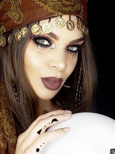 a woman with dark makeup holding a white ball in her hand and wearing gold jewelry