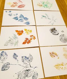 four different colored leaves on white cards sitting on top of a wooden table next to each other