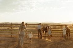 a group of people standing in front of a fence with horses and a baby on the other side