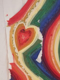 a heart shaped piece of cloth on top of a white tablecloth covered in multicolored strips