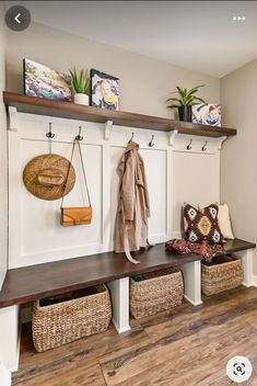 a bench with baskets and coat hooks on it in a home entryway that has wood flooring and white painted walls