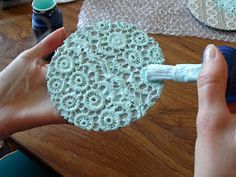 a person using a brush to paint a doily on a wooden table with other craft supplies