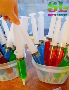 a hand is picking up some plastic straws from a container filled with colored liquids