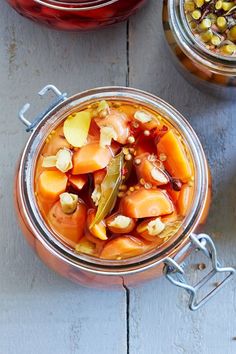 two jars filled with pickled vegetables on top of a wooden table next to spoons