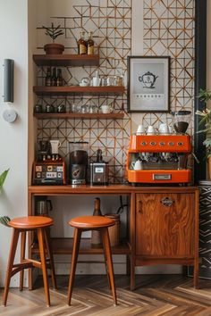 an orange coffee machine sitting on top of a wooden table next to two stools