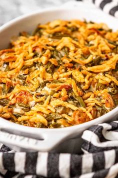 a white casserole dish filled with green beans and cheese on a black and white striped towel