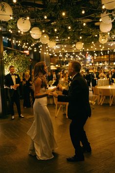 a bride and groom dance together at their wedding reception in an indoor venue with string lights hanging from the ceiling