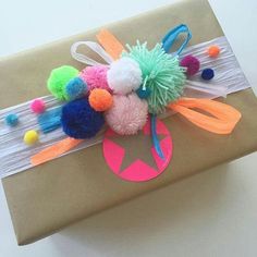 a gift wrapped in brown paper with pom - poms