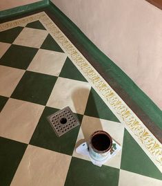 a coffee cup sitting on top of a green and white checkered floor next to a grate