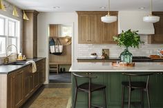 a kitchen with green cabinets and white marble counter tops, two bar stools in front of the island