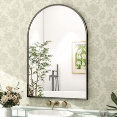 a bathroom sink sitting under a mirror next to a vase with flowers on top of it