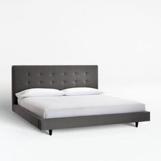 an upholstered bed with white sheets and grey headboard, in front of a white wall