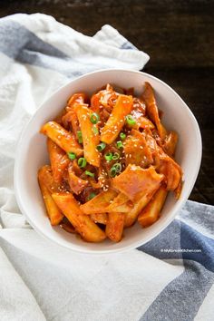 a white bowl filled with pasta covered in sauce and green onions next to a napkin