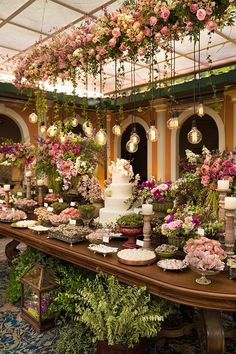 a table covered in lots of flowers next to a wall filled with potted plants