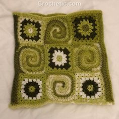 a green crocheted square with white and black flowers on it, sitting on a bed