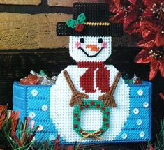 a cross stitch snowman sitting on top of a blue box filled with candies