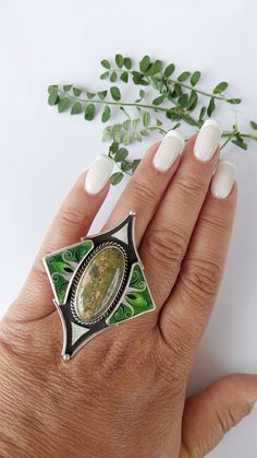 Introducing our stunning Silver Cloisonné Enamel Ring, featuring a captivating Unakite stone at its center. This exquisite piece of jewelry combines the intricate artistry of Cloisonné enamel with the natural beauty of Unakite, creating a truly unique and elegant accessory. The ring's design showcases vibrant green enamel accents that beautifully complement the earthy tones of the Unakite stone. Handcrafted with meticulous attention to detail, the silver setting enhances the overall elegance of the piece, making it a standout addition to any jewelry collection. Perfect for those who appreciate fine craftsmanship and natural gemstones, this ring is more than just an accessory--it's a statement of style and sophistication. Whether worn for special occasions or as an everyday adornment, this Art Deco Enamel Ring As A Gift, Art Deco Enamel Ring As Gift, Art Deco Enamel Jewelry Ring, Art Deco Enamel Ring Jewelry, Adjustable Green Enamel Jewelry, Green Sterling Silver Art Deco Jewelry, Green Round Inlay Jewelry, Artisan Adjustable Green Jewelry, Adjustable Green Artisan Jewelry