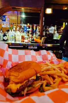 a hamburger and french fries on a checkered table cloth in front of a bar