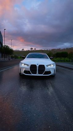 a white car is driving down the road at dusk with clouds in the sky behind it