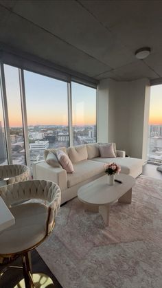 a living room filled with furniture and large windows overlooking the cityscape at sunset