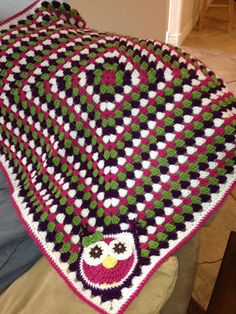 a crocheted blanket with an owl sitting on it's side next to a bed