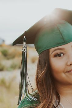 a young woman wearing a green graduation cap and gown smiling at the camera with her hand on her hip