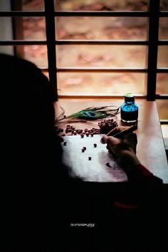 a person sitting at a table writing on a piece of paper next to a bottle