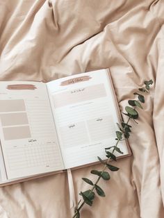 an open planner book sitting on top of a bed next to a green leafy plant