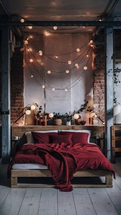 a bed with red sheets and lights hanging from the ceiling in front of a brick wall