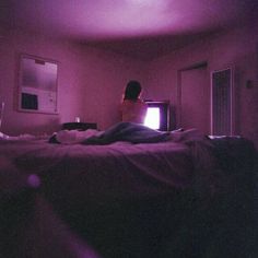 a woman is sitting on her bed watching tv in the dark with purple light coming from behind