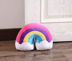 a rainbow shaped pillow sitting on the floor in front of a door with white trim