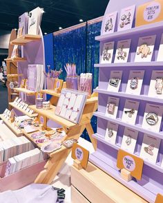 an assortment of items on display in a store with purple walls and wooden shelves holding greeting cards