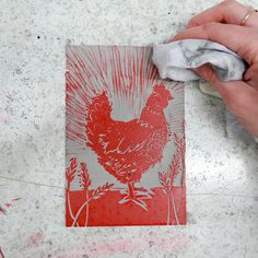 a hand is holding a piece of paper with a red rooster on it