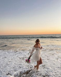 a woman in a white dress is walking into the water at sunset on the beach