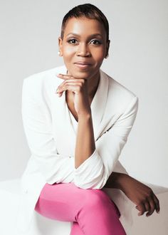 a woman sitting on top of a white couch wearing pink pants and a white blazer