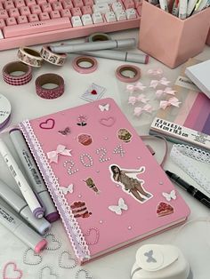 a pink notebook sitting on top of a desk next to some pens and pencils