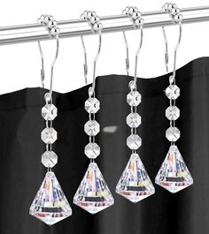 three pairs of earrings hanging from a metal bar on a shower curtain rod with black curtains behind it